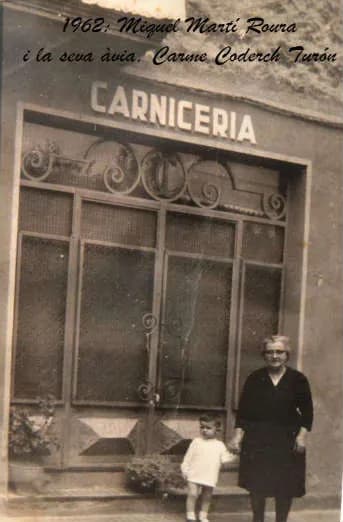 Miquel Martí Roura, de nen, amb la seva àvia Carme Coderch Turón davant la carnisseria (1962)