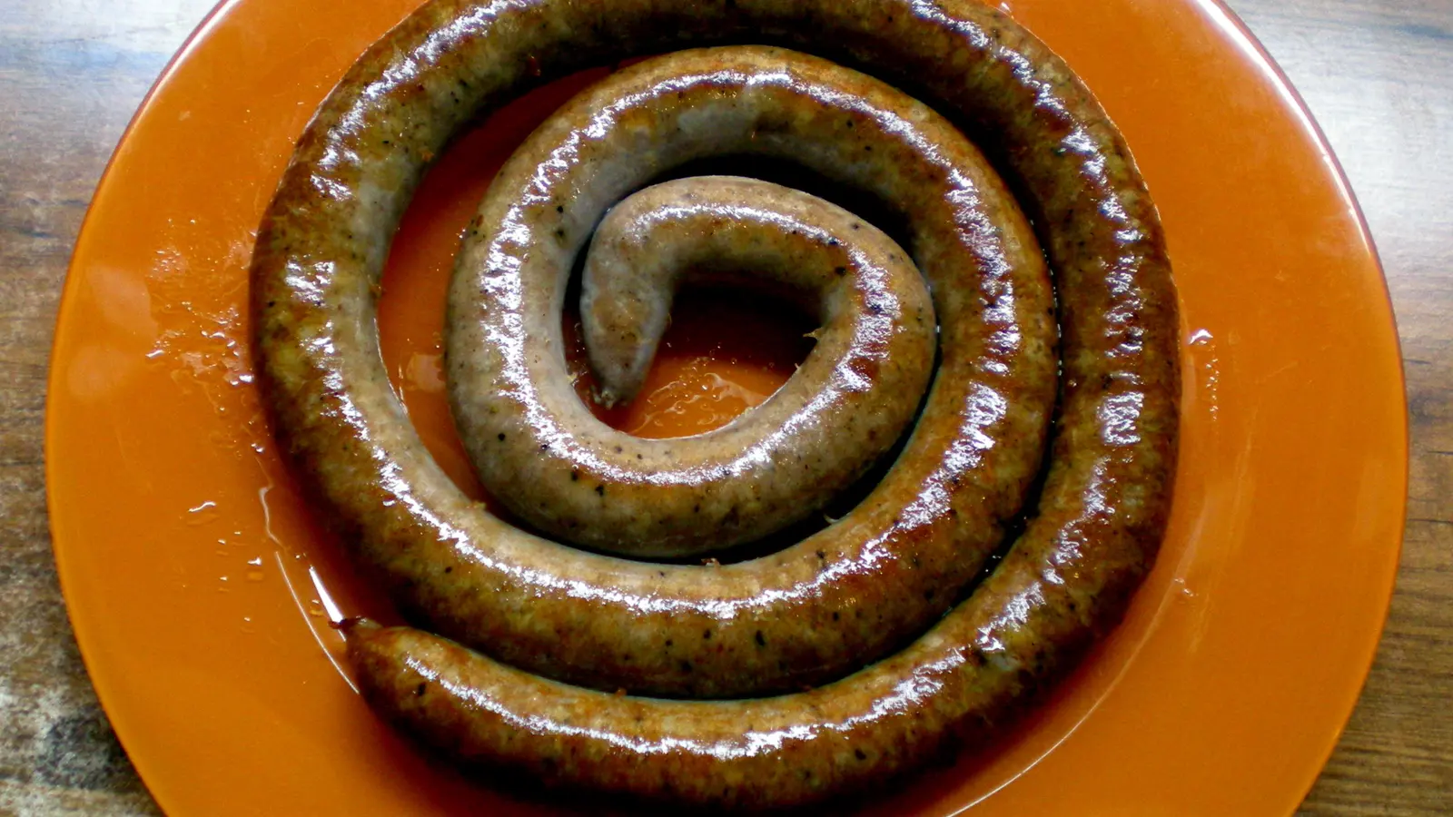 Botifarra fresca enrotllada en espiral sobre un plat taronja